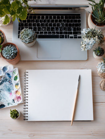 A vibrant desk setup invites creativity with a sketchpad, a paintbrush, a laptop, and lush plants arranged thoughtfully for artistic inspirationの素材