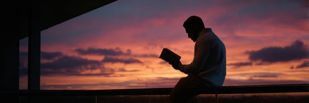 A student sits on a balcony at sunrise, absorbed in a motivational book, as the sky appears clear with vibrant colors illuminating the scene.の素材