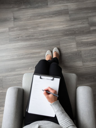 A person is seated comfortably in a minimalist interior, taking notes during a personal coaching session, fostering self-improvement and focus.の素材