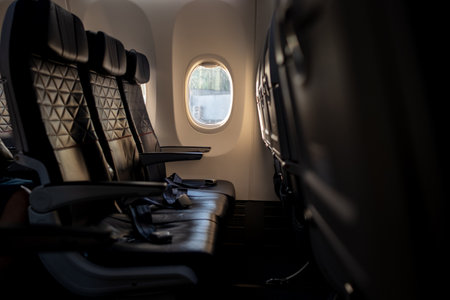 Rows of empty seats in an airplane reflect the warm glow of sunlight through the window, creating a...