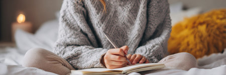 A young woman journals on her bed, illuminated by a warm lamp in a cozy room, embracing self-reflection and tranquility.の素材