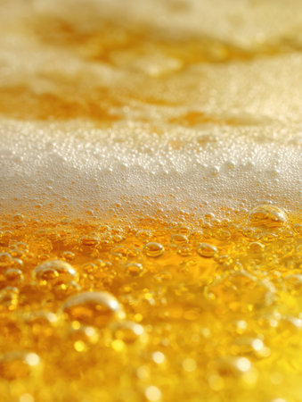 Sparkling golden beer surface features a frothy foam layer, with bubbles rising amidst a blurred top zone, showing a refreshing beverage experience.の素材