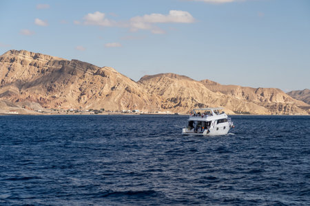 A motorboat glides over blue waters, framed by rugged desert mountains under a clear sky in the...