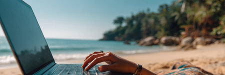 A person is using a laptop on a sandy beach, enjoying the sun and ocean breeze, with palm trees in the background and waves gently crashing.の素材