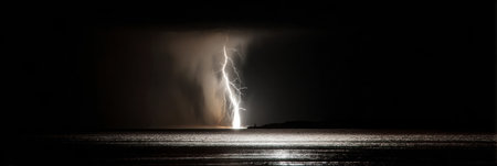 Bright lightning illuminates a dark sky over the ocean, creating a striking contrast as it strikes the water during a powerful nighttime storm.の素材