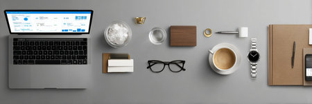 A neatly organized workspace with a laptop, coffee cup, stationery, and glasses on a gray desk, creating a productive atmosphere for work.の素材