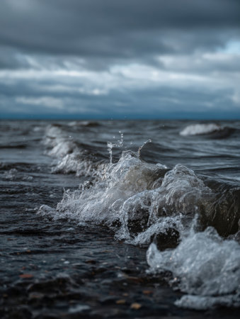 Waves crash onto a rocky shoreline as dark clouds gather overhead during the early evening, creating a dramatic atmosphere on the water.の素材