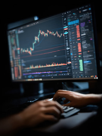 In a dimly lit room, a person is focused on analyzing cryptocurrency charts and market data on a computer screen while trading at night.の素材