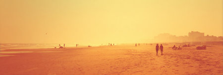 People walk along a sandy beach at sunset, enjoying the warm glow while others relax or engage in activities against a city skyline backdrop.の素材