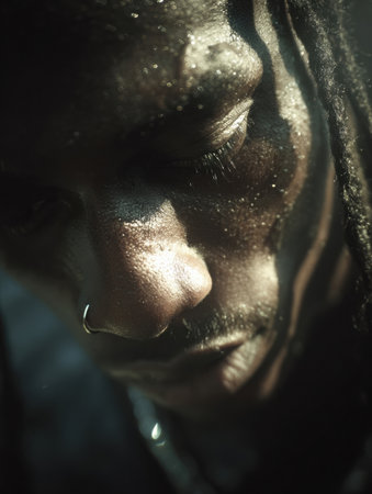 A man with dreadlocks gazes downwards, lost in deep contemplation, illuminated by soft, diffused lighting highlighting his features.の素材