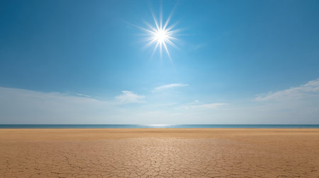 A desolate, cracked earth surface stretches toward the ocean, with a bright sun shining overhead and few clouds in the clear blue sky.の素材