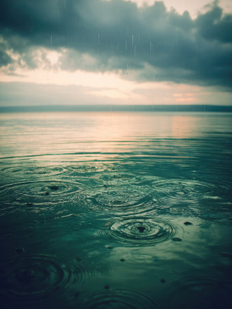 Gentle rain creates ripples on the tranquil surface of a lake, reflecting the moody clouds overhead during the peaceful evening.の素材