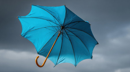 A vibrant blue umbrella lifts off the ground, spinning in the air as strong winds blow through the scene filled with dark, ominous clouds.の素材