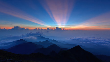 Vibrant rays of sunlight break through clouds as dawn emerges over a rugged mountain range, creating a stunning visual display in the early morning.の素材