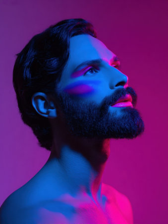 A man poses with an upward gaze, showcasing bold blue and pink face paint against a vivid backdrop, creating a striking artistic effect in a studio.の素材
