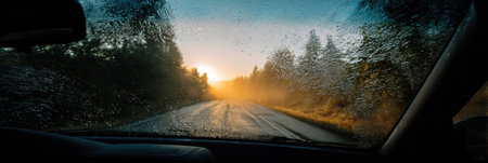 Driving along a quiet road at dawn with sunlight filtering through the fogged-up windshield, creating a serene atmosphere in nature.の素材