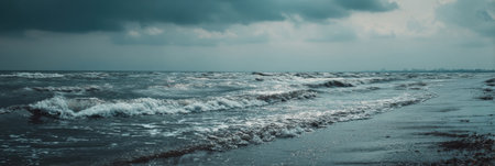 Rough waves pound the shoreline as dark clouds gather above, creating a moody atmosphere in the late afternoon at a coastal location.の素材