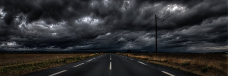 Dark, ominous clouds loom over a deserted road, signaling a storm approaching in the late afternoon. The landscape features open fields on either side.の素材
