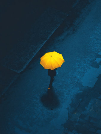 A figure walks alone on a dimly lit street, holding a bright yellow umbrella against the rain during a gloomy evening. Reflections glisten on the pavement.の素材