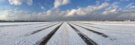 A wide snow-covered airstrip stretches under a dramatic sky, featuring clouds and patches of blue, typical of a winter afternoon setting.の素材