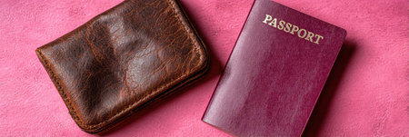 A brown leather wallet and a maroon passport are placed together on a pink background, highlighting key items for travel preparations.の素材