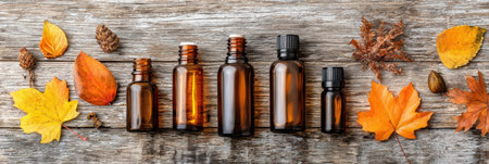 Various amber glass bottles arranged alongside vibrant autumn leaves and pine cones on a textured wooden background create a seasonal aesthetic.の素材