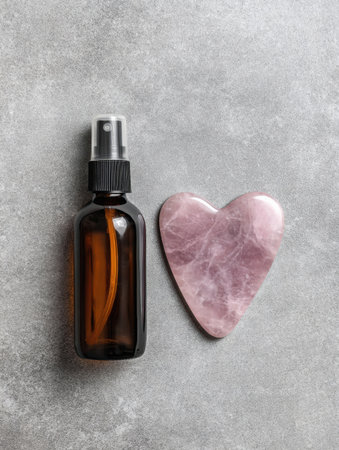 Amber spray bottle placed next to a heart-shaped jade tool highlights a wellness setup, perfect for skincare enthusiasts focusing on self-care rituals.の素材