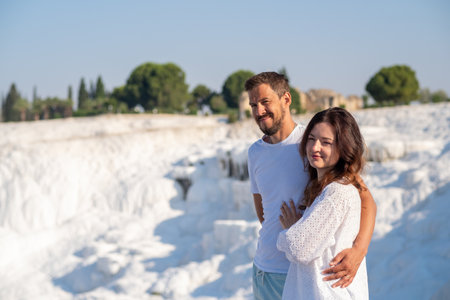 Beautiful couple stands together at Pamukkale, admiring the stunning white travertine terraces and warm thermal waters in a sunny, serene setting.の写真素材