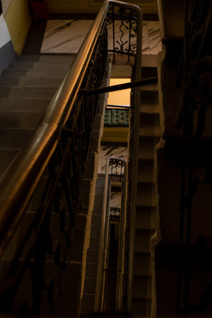 An ornate staircase with detailed railing leads downward within a historic structure, illuminated softly by ambient light, suggesting a cozy atmosphere.の写真素材