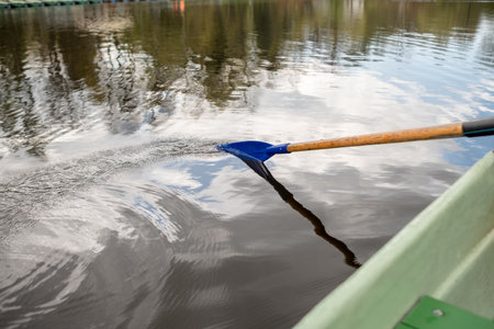A person paddles a boat on serene water, creating ripples while trees are mirrored in the surface under a clear sky during midday.の写真素材