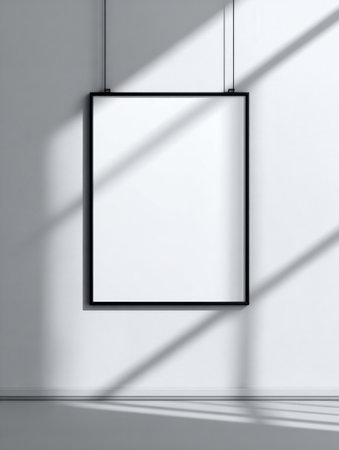 A large black frame without artwork hangs on a white wall, cast in shadows from sunlight streaming through a window in the afternoon.の素材