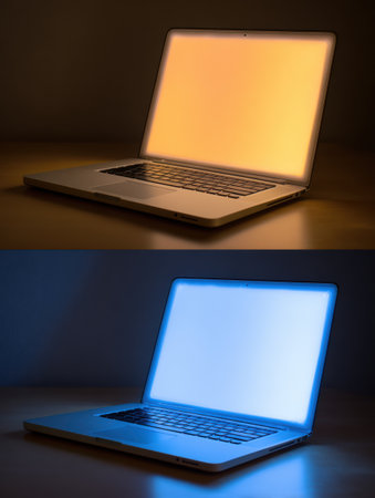 A laptop sits on a wooden surface, illuminated from the screen in warm yellow and cool blue light, creating a visually striking contrast in colors.の素材