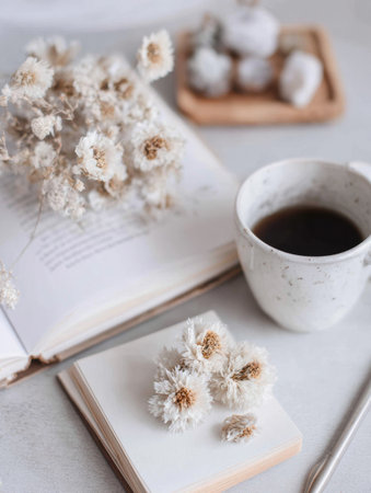 A warm setting features a cup of coffee beside dried flowers and an open book, creating a tranquil atmosphere perfect for relaxation and reflection.の素材