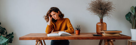 Woman in a mustard sweater sits at a wooden desk, focused on her studies amidst a serene atmosphere, surrounded by plants and decor.の素材