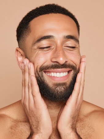 A man is smiling brightly gently while touching his face, showcasing a well-groomed beard against a soft, warm background that evokes comfort.の素材
