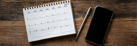 A notepad with a weekly planner open beside a smartphone and a silver pen, resting on a rustic wooden table. Ideal for organizing tasks.の素材