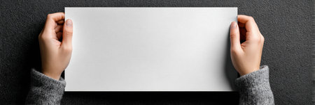 Two hands grip a blank sheet of white paper against a dark background, creating a striking contrast and emphasizing the simplicity of the scene.の素材