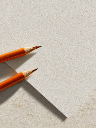 Two orange pencils lie beside a blank sheet of white paper on a neutral textured surface, creating a welcoming atmosphere for artistic endeavors.の素材
