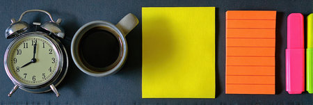 A vintage clock shows early morning time next to a coffee cup, colorful sticky notes, and highlighters on a dark workspace, creating a productive atmosphere.の素材