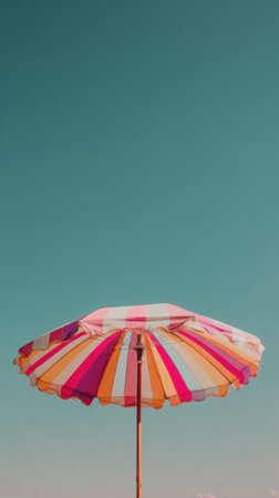 A colorful striped beach umbrella stands tall against a bright blue sky, offering a perfect shade on a sunny summer day at the beach.の素材