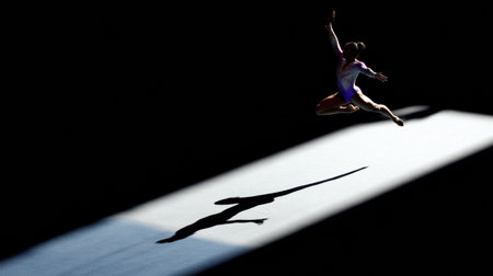 Athlete executes an impressive jump surrounded by darkness, with a focused beam of light illuminating the performance during an evening gymnastics event.の素材
