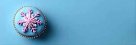 A beautifully decorated cupcake topped with a pink and white snowflake sits on a smooth, light blue background, evoking a winter theme.の素材