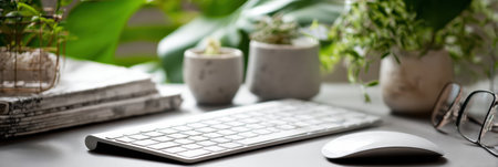 A workspace features a sleek keyboard and mouse positioned next to small potted plants and stacked reading materials, creating a tranquil atmosphere.の素材