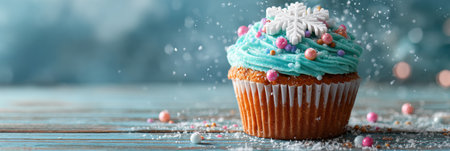 Winter-themed cupcake vibrant features blue frosting, decorative snowflakes, and colorful sprinkles, creating a festive treat on a rustic wooden table.の素材
