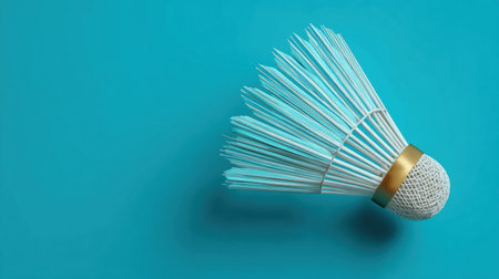 A shuttlecock lies on a vibrant turquoise background, emphasizing its feathers and cork base, commonly used in badminton activities and games.の素材