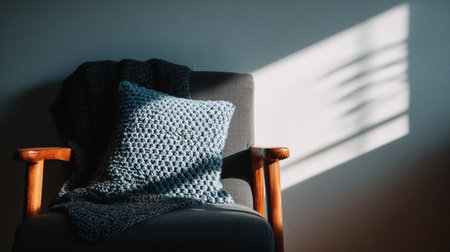 Soft afternoon light casts a gentle shadow on a cozy chair draped with a knitted blanket and pillow, creating a warm, inviting atmosphere.の素材