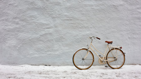 A vintage bicycle stands elegantly against a smooth white wall, showing its charming design in a serene urban environment during the day.の素材