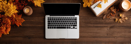 A laptop sits open on a rustic wooden table adorned with colorful autumn leaves and candles creating a warm, inviting atmosphere for creativity.の素材