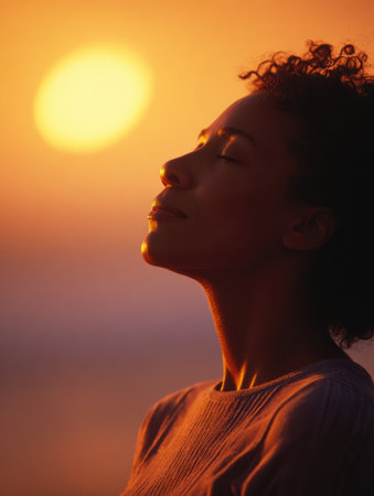 A woman sits outdoors, eyes closed and calm, meditating at sunset.の素材