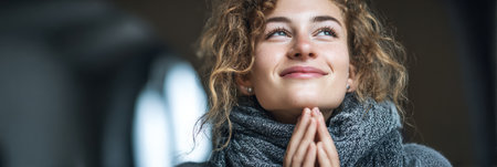 Woman with curly hair and gray scarf smiles while reflecting on the benefits of gratitude, promoting mental well-being and a positive outlook.の素材